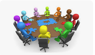 Colorful 3D figures sit around a round table, each holding puzzle pieces, suggesting teamwork and collaboration.