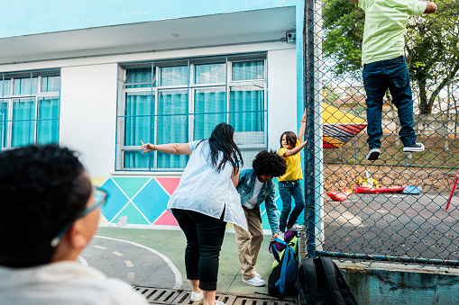 Image shows children deliberately climbing a metal fence with a teacher encouraging them down.